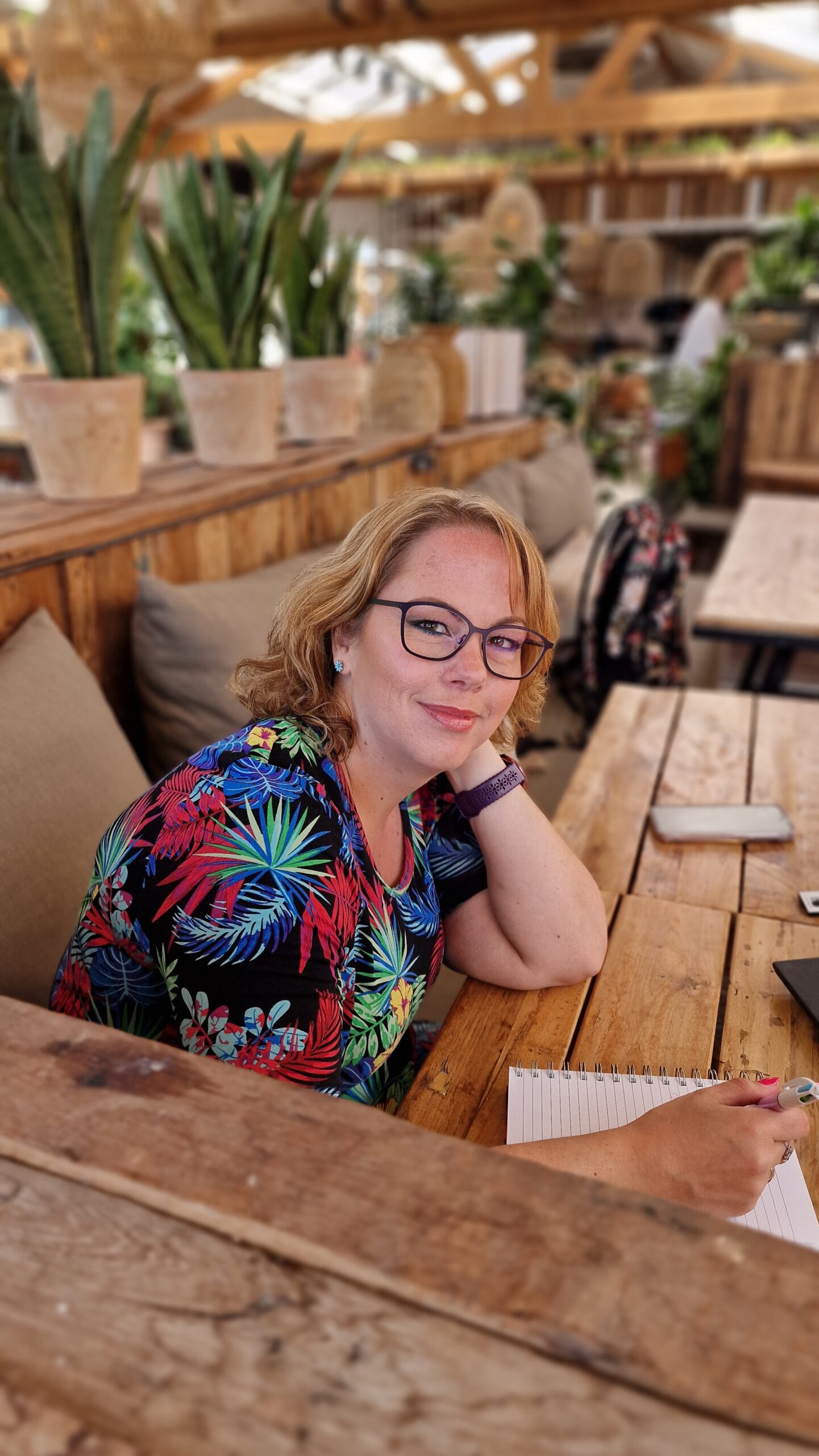 Mandy, een vrouw met bril en een vrolijke jurk aan, werkend met pen, papier en laptop